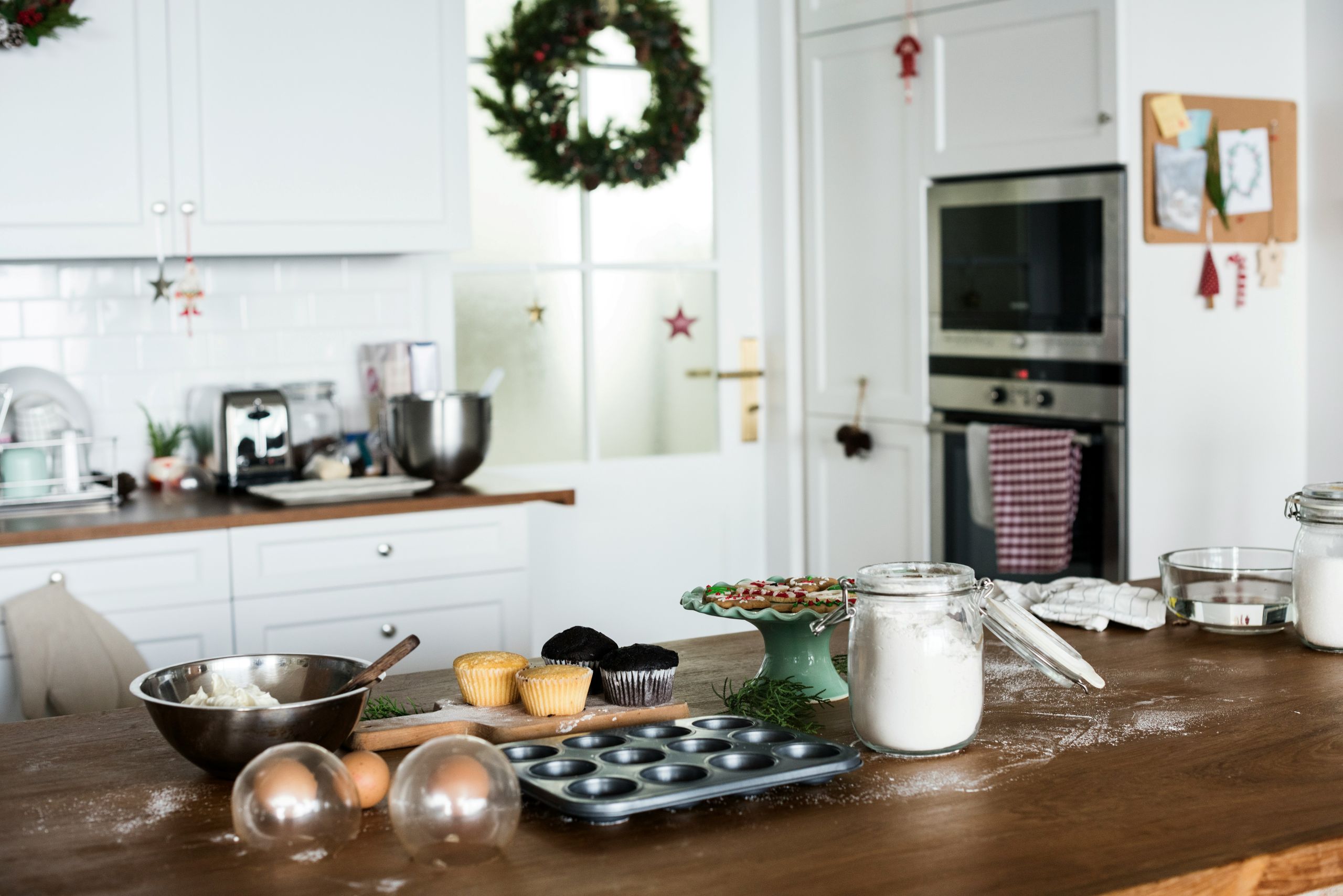 pests A kitchen with baking supplies on a wooden counter, including flour, cupcakes, mixing bowls, and utensils. Christmas wreaths and decorations hang in the background, creating a festive atmosphere free from pests.