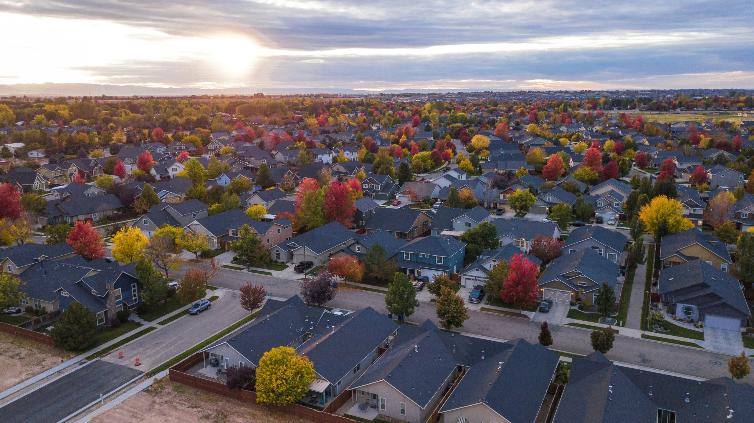 Aerial view of a suburban neighborhood at sunset, with houses lined in rows and trees displaying vibrant autumn colors.
